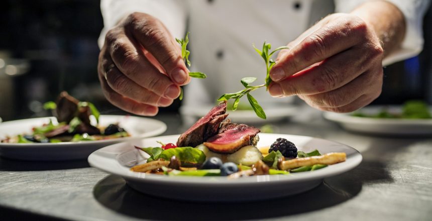 Chef adding the final flourish by adding some liquorice flavoured  parsley to the dish. The dish is, pan fried pink duck breast onto a bed of parsnip puree with seasonal autumn vegetables and berries. Colour, horizontal with some copy space, photographed on location in a restaurant on the island of Møn in Denmark.
