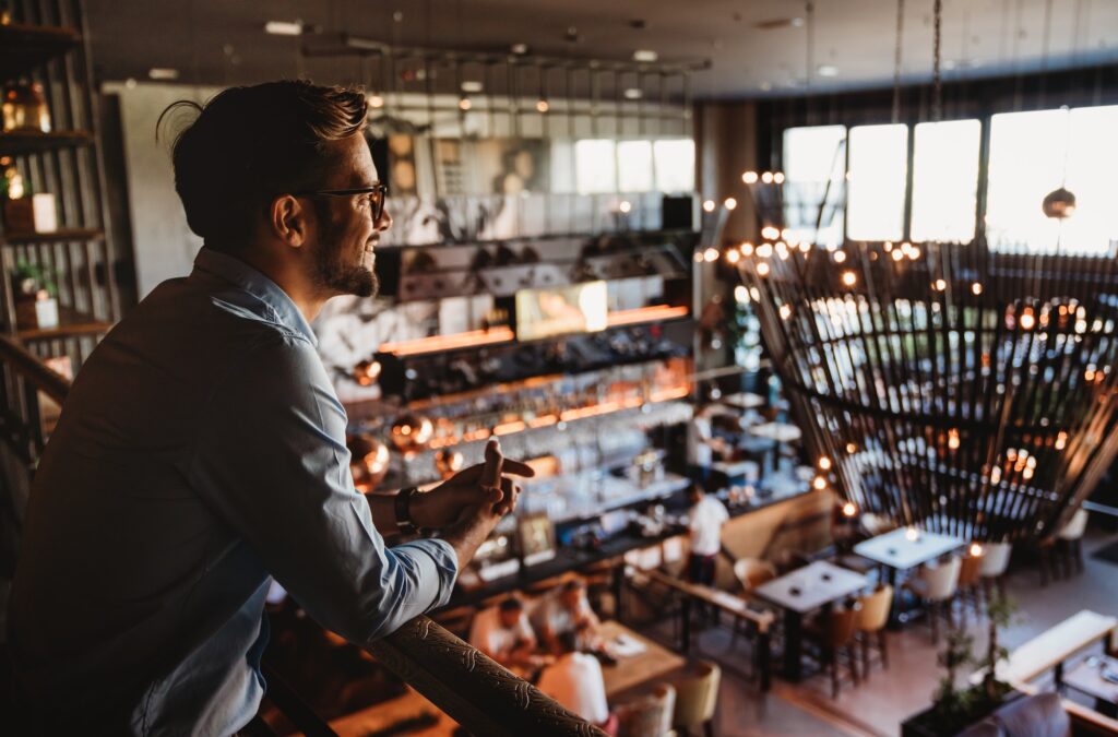 Happy businessman, restaurant owner proudly looking at crowded restaurant